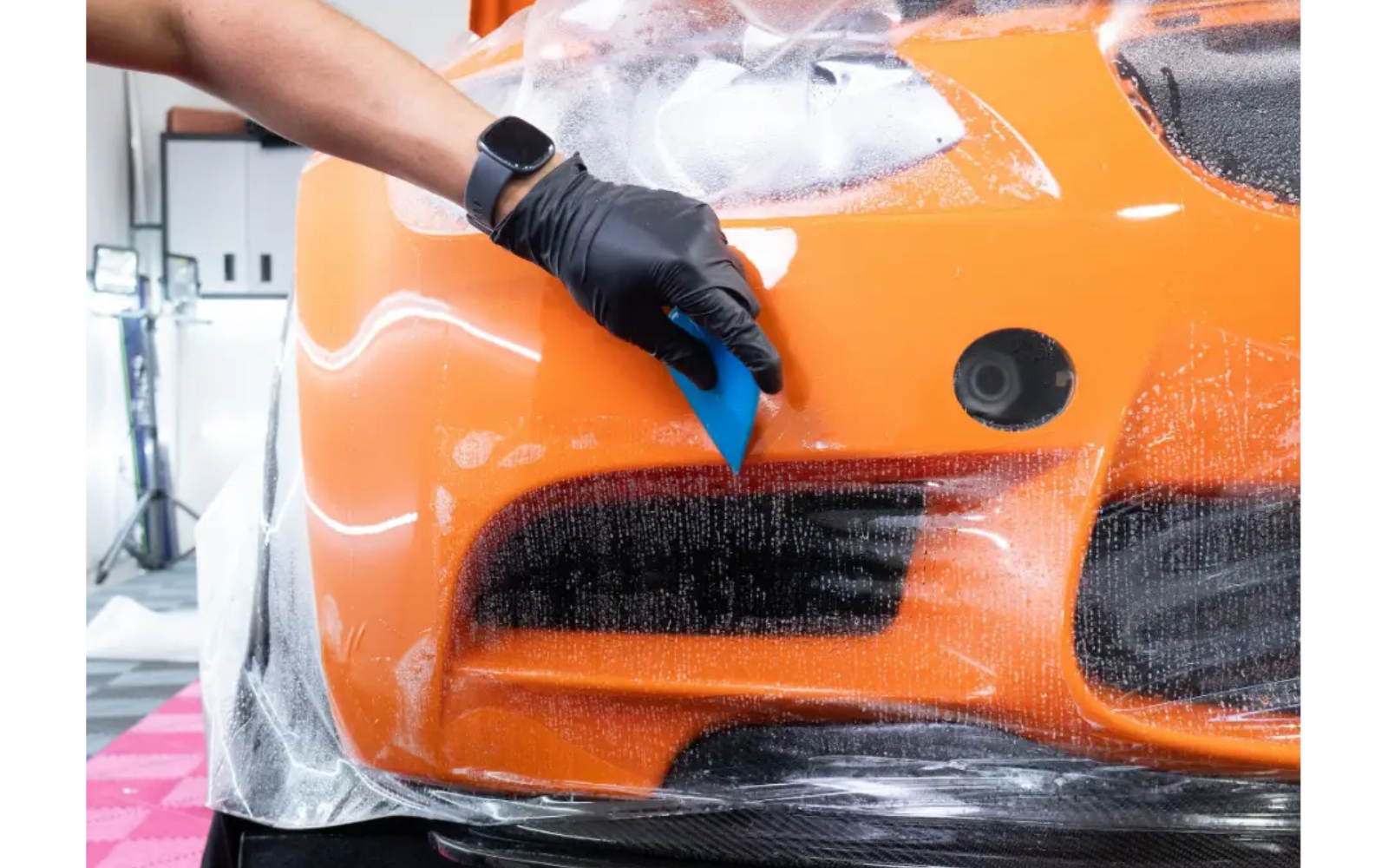 Gloss PPF install — squeegee laying film on an orange supercar bumper