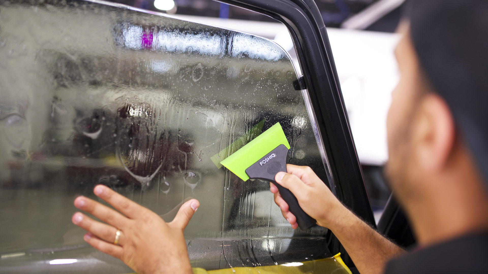 Window tint installer squeegeeing slip solution out from under fresh KAVACA film on a side window at Ceramic Pro Fuel House