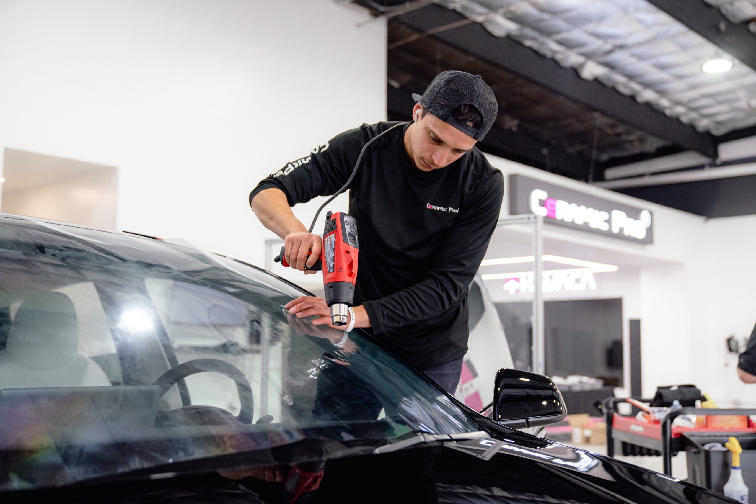 Ceramic Pro technician heat-shaping clear KAVACA windshield protection film over a Tesla windshield at Ceramic Pro Fuel House